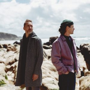 Visuel de tournée pour Sula Bassana.
En fond, une falaise, des roches, le tout surplombant l'océan. Le ciel est couvert de quelques nuages blancs.
Légèrement à gauche du centre, le saxophoniste Christophe Panzani. Il porte un sweet noir et un épais manteau gris qui lui arrive en haut des cuisses. Légèrement à droite du centre, le producteur 20syl. Il a le regard tourné vers l'horizon et les mains dans les poches de son pantalon. Il porte un bonnet vert foncé, un pull bleu marine et une veste en jean mauve.