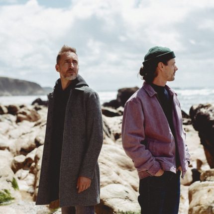 Visuel de tournée pour Sula Bassana. En fond, une falaise, des roches, le tout surplombant l'océan. Le ciel est couvert de quelques nuages blancs. Légèrement à gauche du centre, le saxophoniste Christophe Panzani. Il porte un sweet noir et un épais manteau gris qui lui arrive en haut des cuisses. Légèrement à droite du centre, le producteur 20syl. Il a le regard tourné vers l'horizon et les mains dans les poches de son pantalon. Il porte un bonnet vert foncé, un pull bleu marine et une veste en jean mauve.